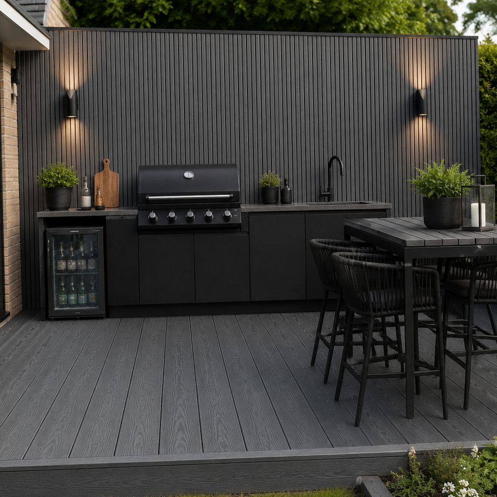 A modern outdoor kitchen setup on a dark gray composite deck, featuring a black gas grill, matching cabinets, a built-in beverage cooler, a dining table with four black bar stools, and a dark gray slatted privacy wall with wall-mounted lights.