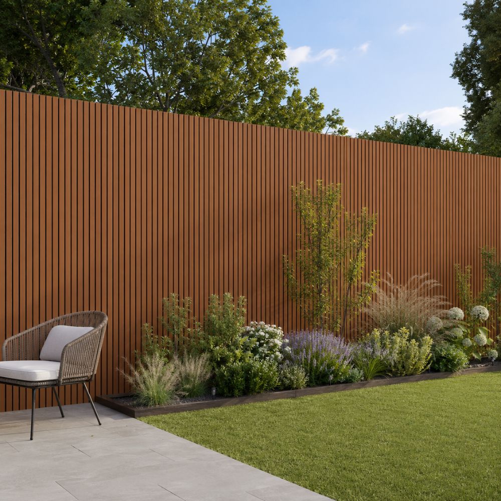 A modern outdoor garden scene with a tall rust-brown slatted privacy fence, a green lawn, landscaped plants, and a wicker patio chair on a light stone patio.