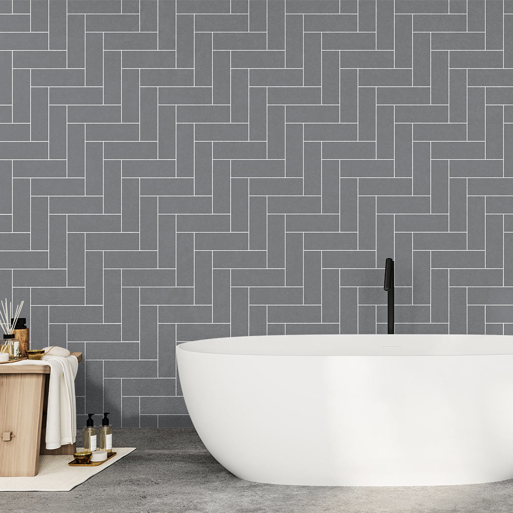 Bathroom with a white freestanding bathtub against a gray herringbone tiled wall.